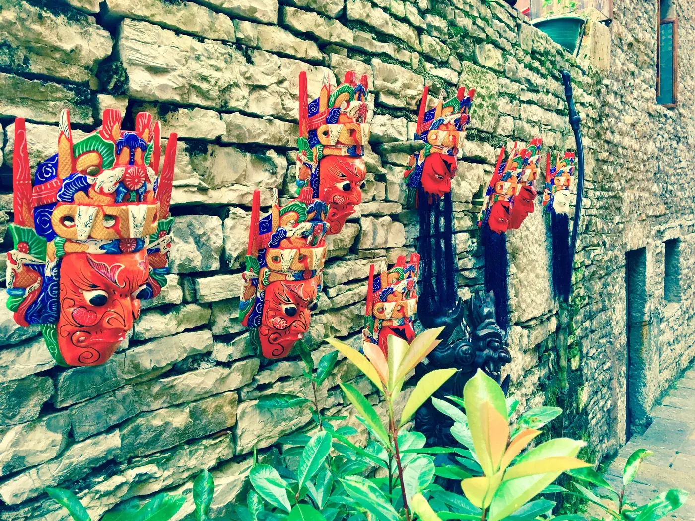 A group of colourful carved masks displayed on a stone wall at Tianlong Tunpu in 2017