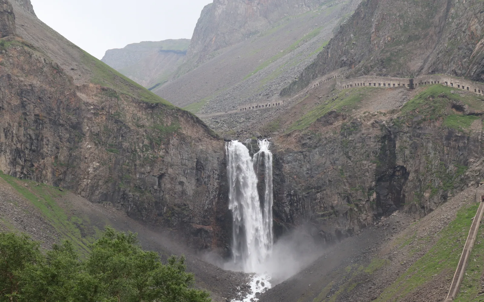 Changbai Waterfall dropping in two streams from a gap in the crater wall into a rocky valley, with a covered walkway along the cliff