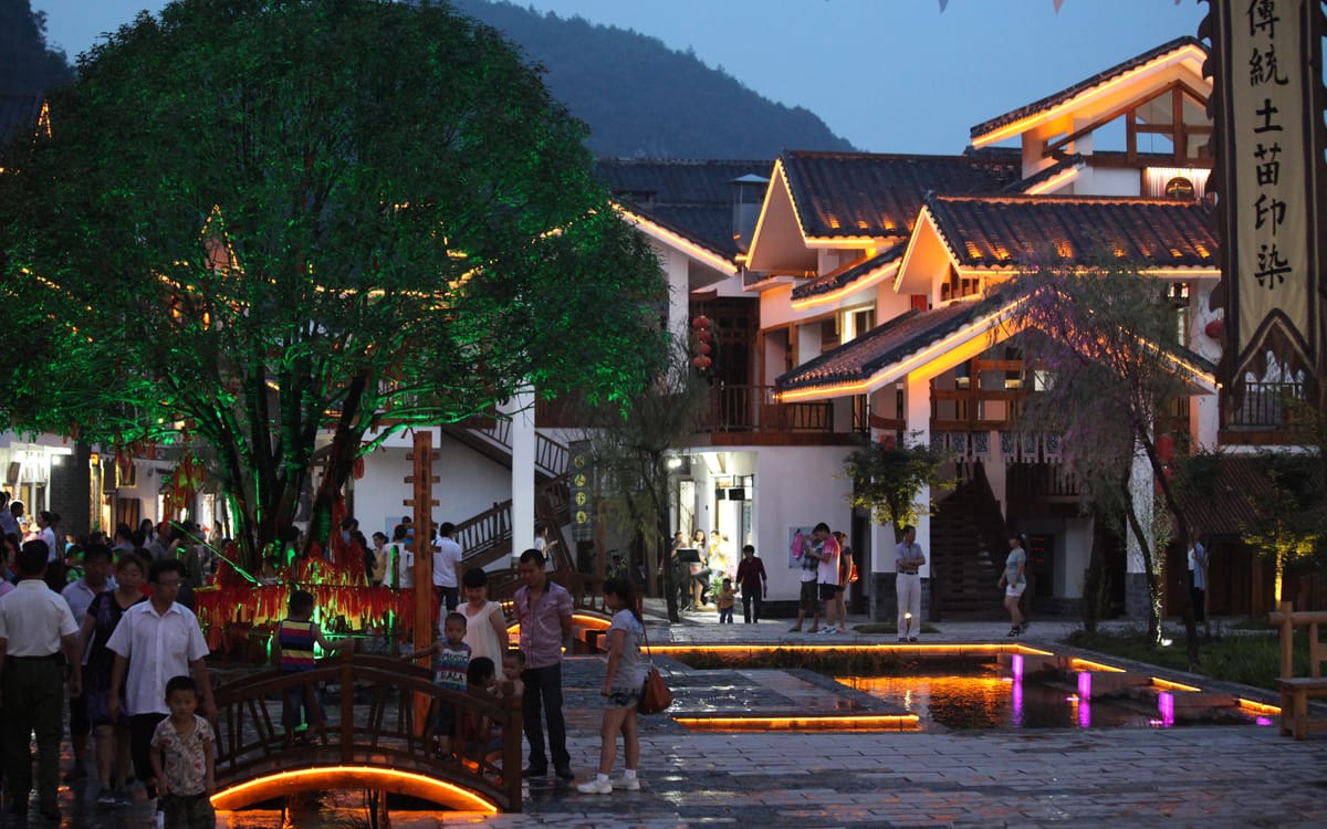 A lantern-lit accommodation and dining street in Zhangjiajie filling with people at dusk.