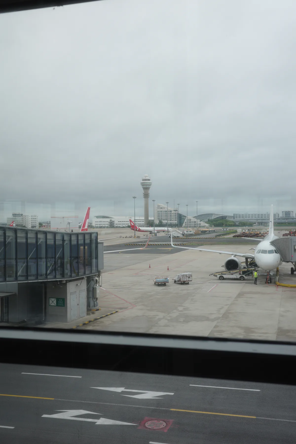 Aircraft on an airport apron beneath grey clouds, seen through a terminal window.