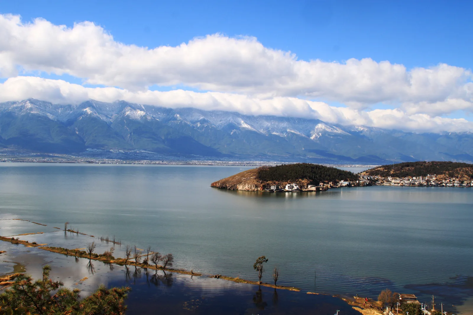 Erhai Lake with a small wooded island, and snow on the Cangshan mountains across the water under a bank of cloud