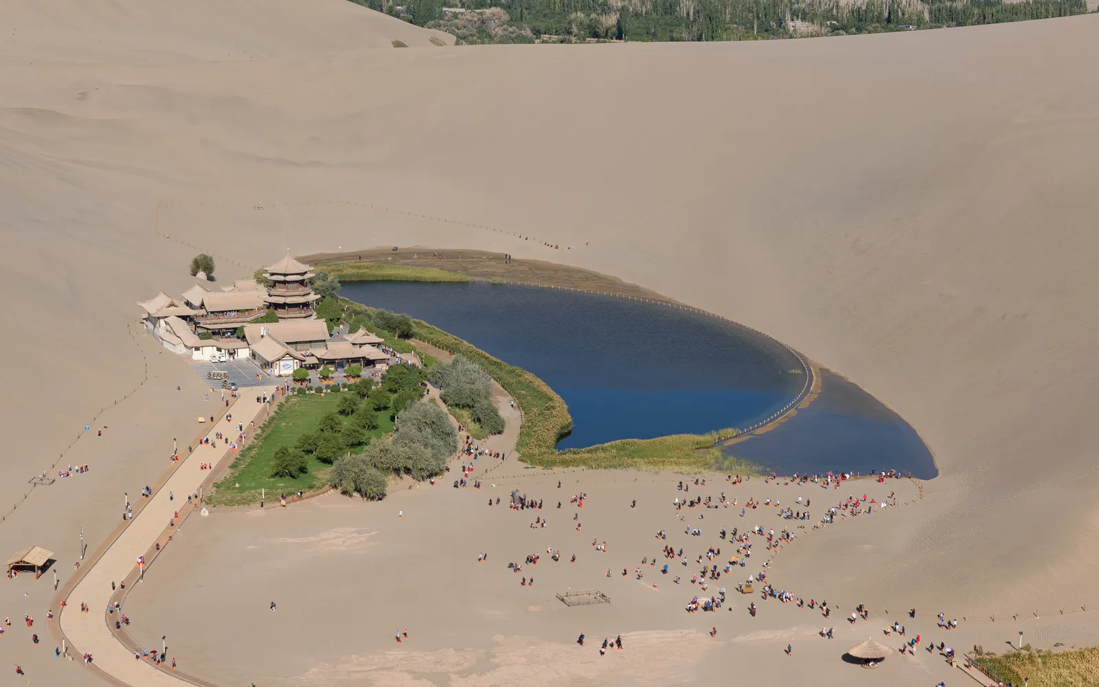 Lac du Croissant et son pavillon vus depuis les dunes de Mingsha, avec des visiteurs en contrebas.