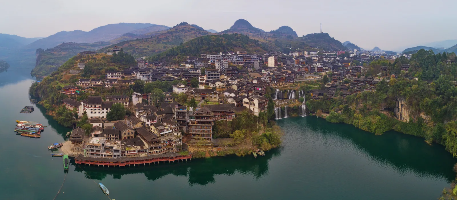 Aerial view of Furong Ancient Town on its headland above the river, with the waterfall dropping from the middle of the town