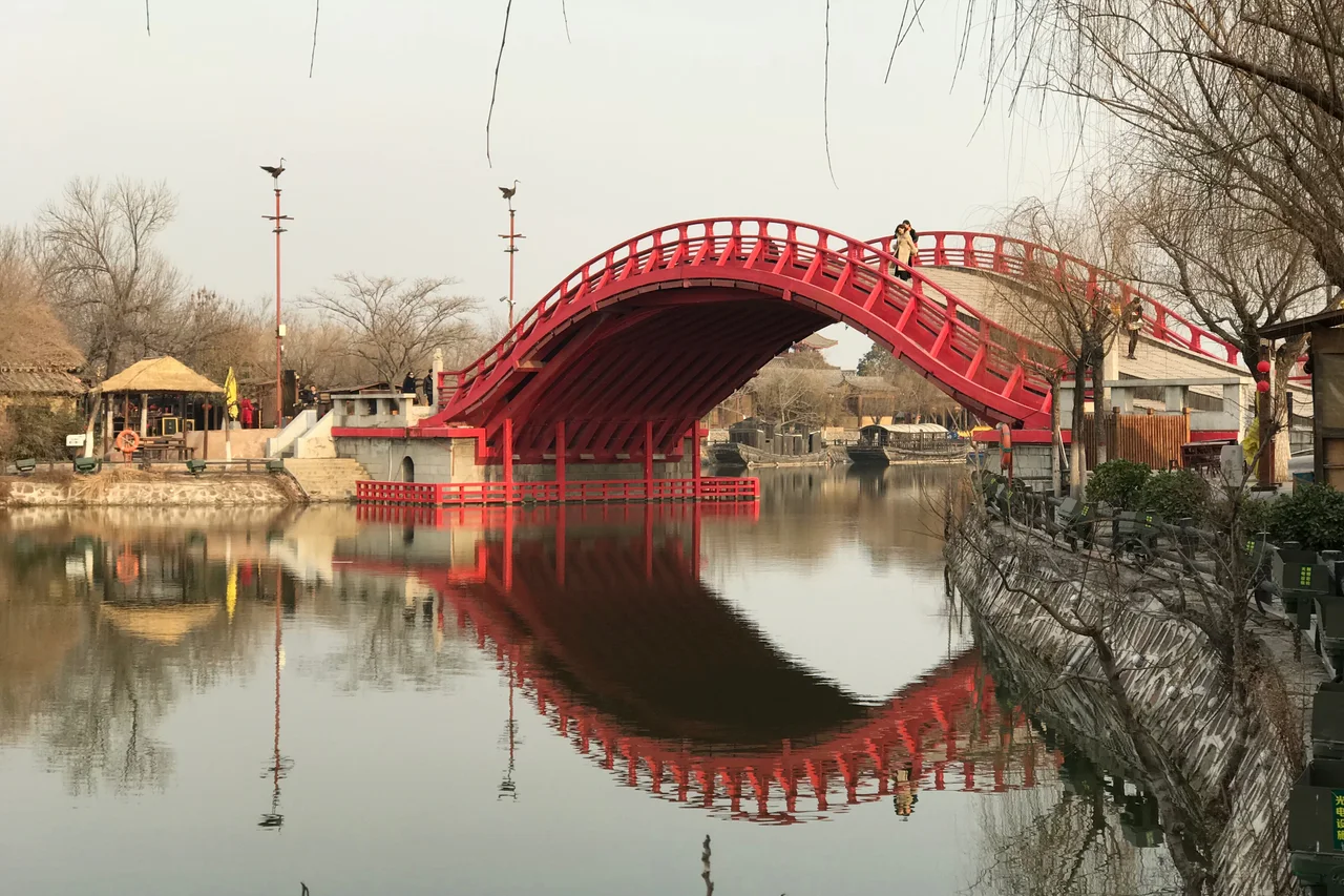 The modern red Hongqiao bridge crossing a waterway inside Qingming Riverside Landscape Garden.