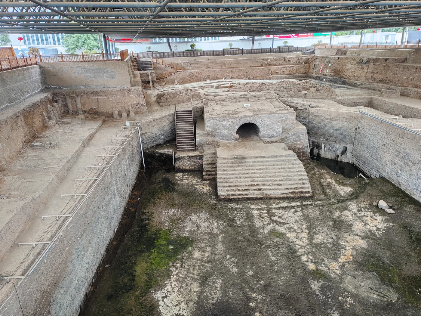 Excavated Zhouqiao site in Kaifeng with exposed masonry bridge remains, canal walls and layered deposits under a protective roof.