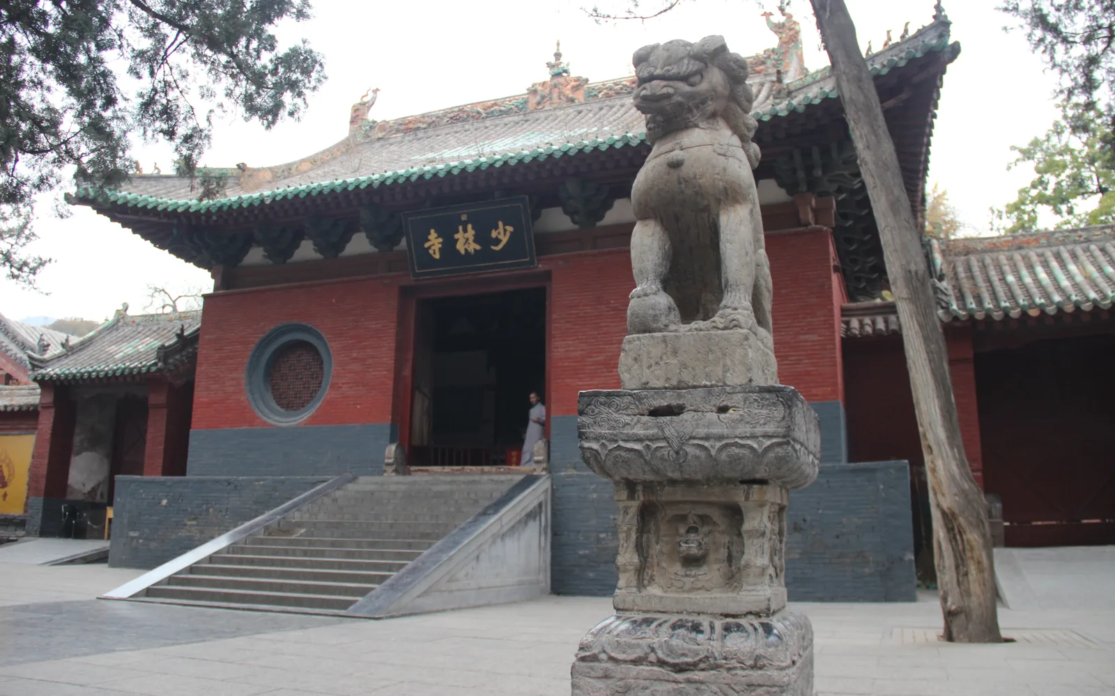 The mountain gate of Shaolin Temple, with red walls and a green-tiled roof, and a stone lion on a carved pedestal in front