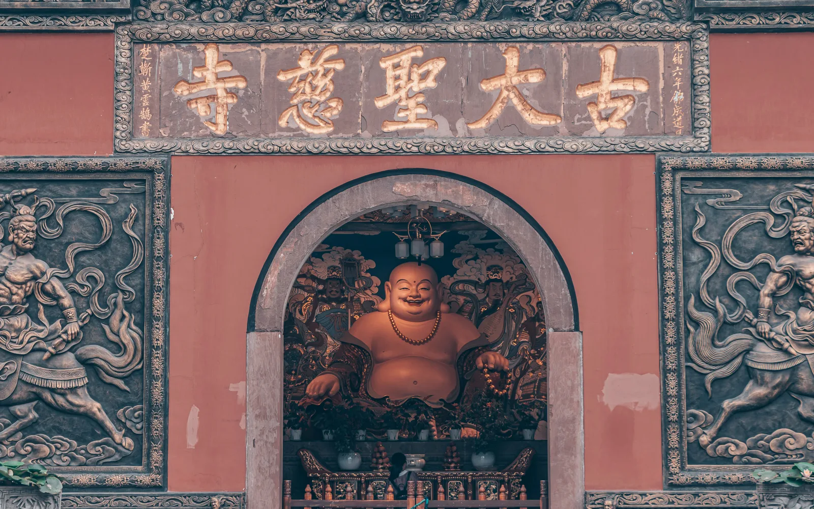 The red gate wall of Daci Temple in Chengdu, with a carved stone arch and a seated Buddha figure inside it