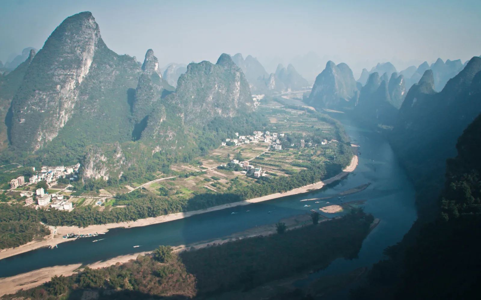 A bend of the Li River between karst peaks and village fields, seen from a hilltop