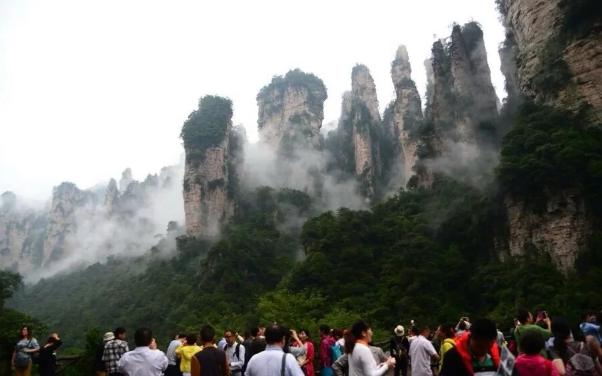 Visitors look toward misty sandstone pillars rising above the forest in Zhangjiajie.