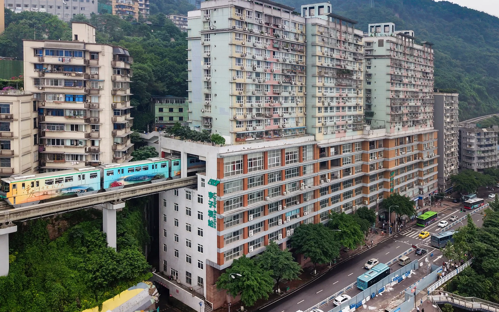A Line 2 train passing through Liziba Station with hillside buildings above and roads below