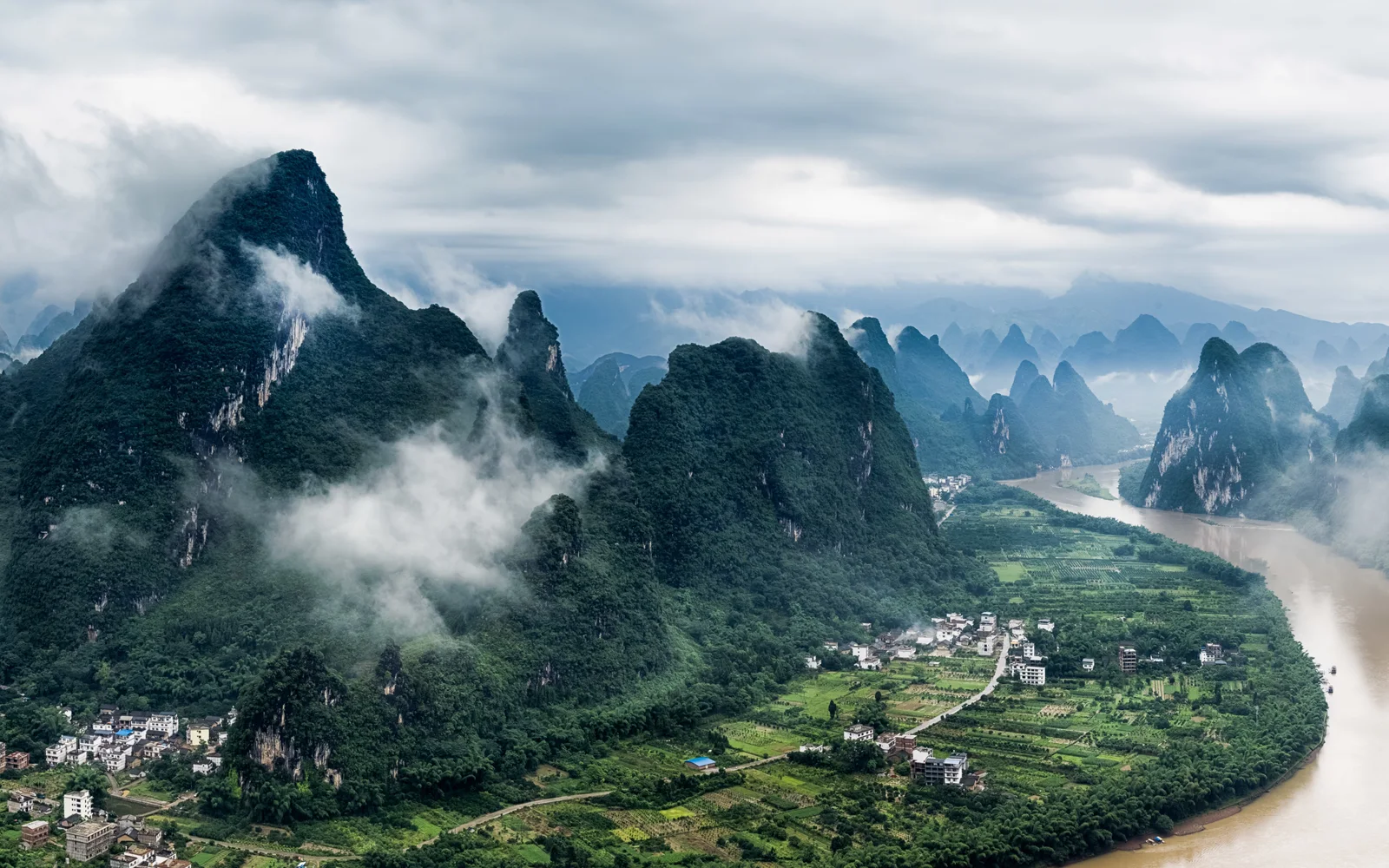 The Li River winding between karst hills near Yangshuo on a cloudy day.