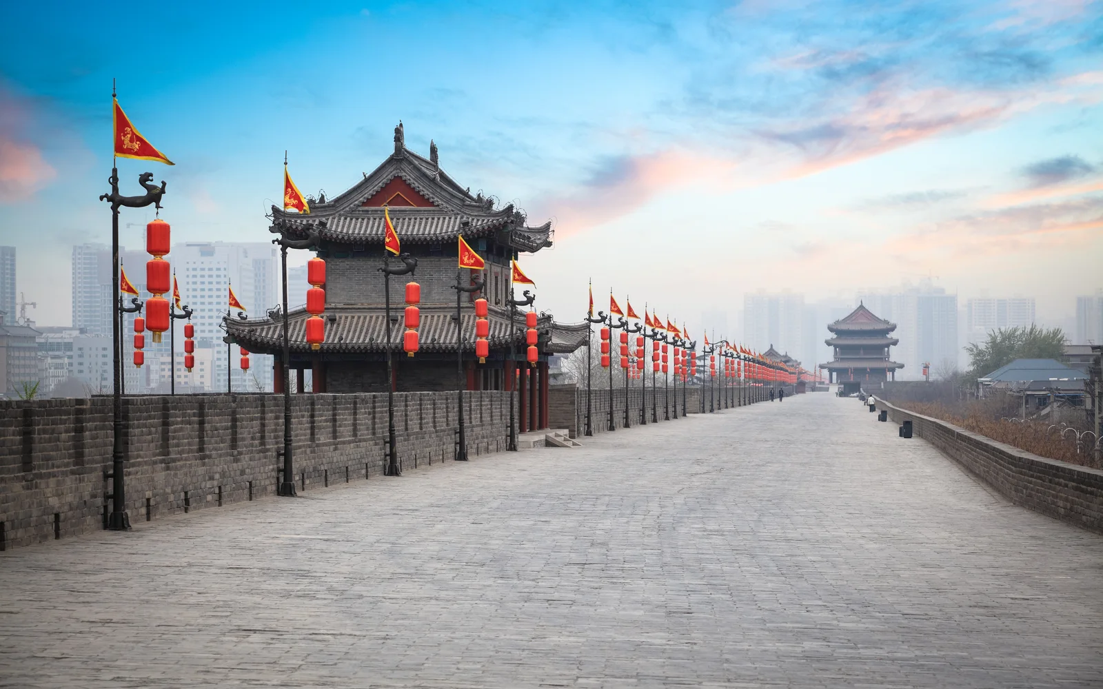 A broad pedestrian stretch on top of Xi'an City Wall at dusk, with a gate tower and lanterns