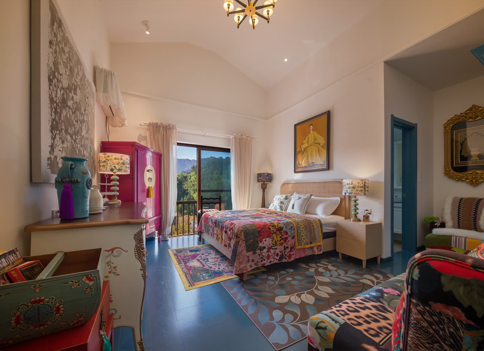 Colourful guest room with one bed, lounge seating and mountains visible through the window