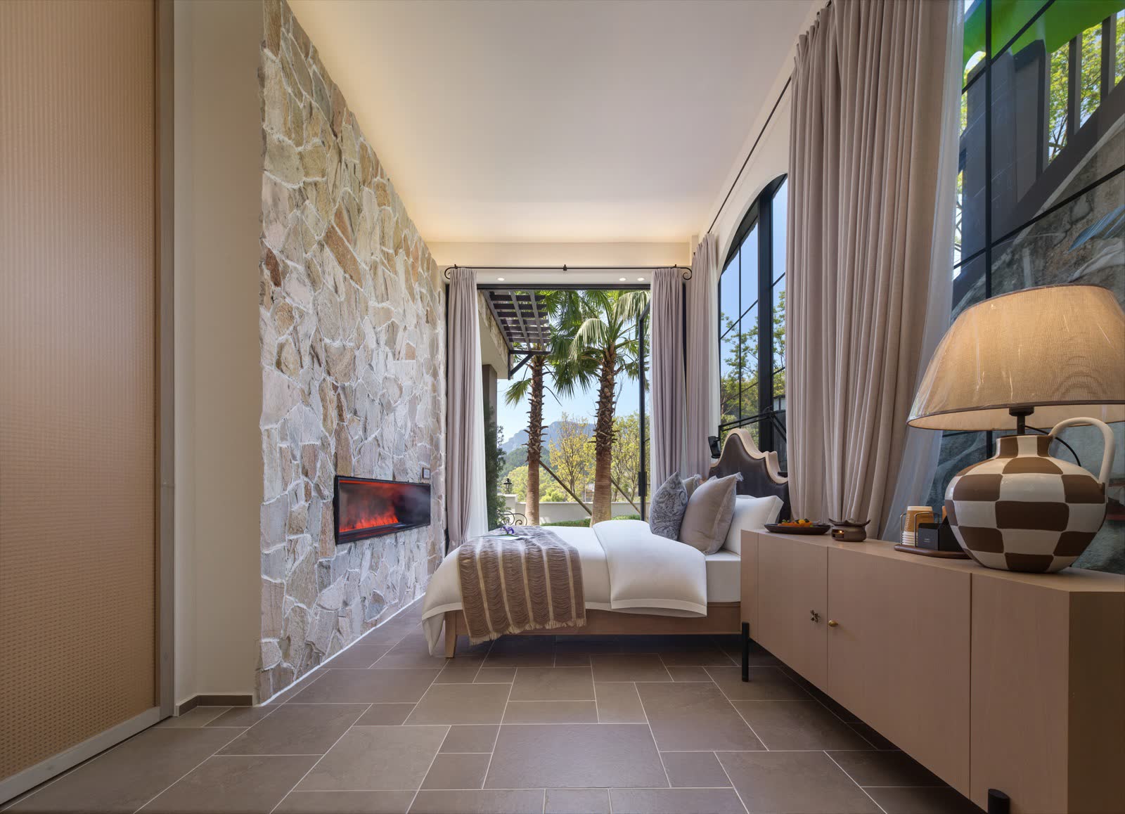 Guest room with a bed, an inset fireplace and greenery outside the windows
